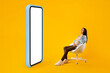 © Prostock-studio - Happy pregnant woman sitting in chair near big smartphone with white screen, looking at copy space for design, mockup