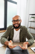 © Prostock-studio - Positive latin bearded man looking at computer screen, having online chat, gesturing and smiling, sitting at desk