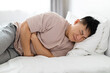 © Prostock-studio - Man lying in bed and suffering from stomach pain
