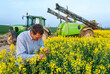 © S. Leitenberger - Traitement insecticide sur colza contre le charancon. Agriculteur observant la présence charancon dans le colza. Pulvérisateur en arrière-plan