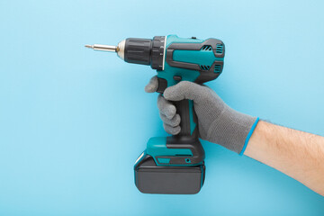 Young adult man hand in protective glove holding and showing dark black green professional battery screwdriver on light blue wall background. Pastel color. Closeup. Tool for repair work. Side view.