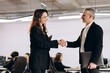 © CinemaF - Smiling businesswoman shaking hands with her business partner. Happy office workers greeting each other in the office. Successful business deal