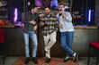 © Serhii - Three young men in casual clothes are smiling, holding bottles of beer while standing near bar counter in pub