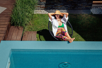 Wall Mural - Full length of a woman wearing sunhat and white shirt while relaxing by the pool