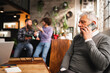 © Pintau Studio - senior businessman talking on the phone sitting at desk in a modern office while colleagues discussing on background.