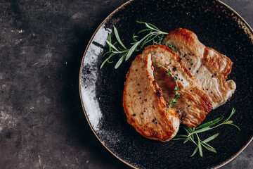 Poster - Fried pork steaks on a black plate on a dark background with rosemary