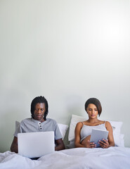 Wall Mural - Dont believe everything you read online. Shot of a couple sitting in bed while using wireless devices.