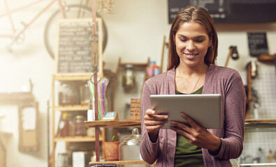 Wall Mural - Keeping a record of her business goals on her tablet. Shot of a young entrepreneur using a digital tablet in her store.