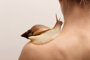 A large achatina snail sits on a woman's shoulder. healthy skin, rejuvenation