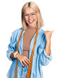 Beautiful young blonde woman dressmaker designer pointing thumb up to the side smiling happy with open mouth