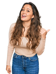 Wall Mural - Young hispanic girl wearing casual clothes smiling with happy face looking and pointing to the side with thumb up.