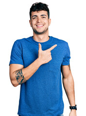 Wall Mural - Young hispanic man wearing casual t shirt cheerful with a smile on face pointing with hand and finger up to the side with happy and natural expression