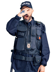 Poster - Young handsome man wearing police uniform peeking in shock covering face and eyes with hand, looking through fingers with embarrassed expression.