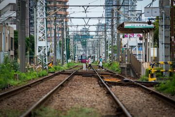 tokyo shitamachi trolly train (toden) running in middle of city and two young asian girls walking ac