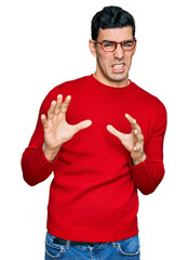 Wall Mural - Handsome hispanic man wearing casual clothes and glasses disgusted expression, displeased and fearful doing disgust face because aversion reaction. with hands raised