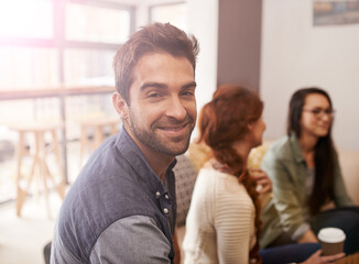 Poster - We all have something in common, coffee. Portrait of a young sitting in a coffee shop with his friends blurred in the background.