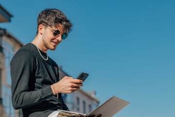 Wall Mural - young man in the street outdoors with laptop and mobile phone