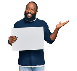 Canvas Print - Young african american man holding blank empty banner celebrating victory with happy smile and winner expression with raised hands