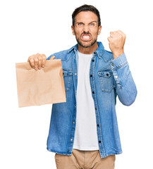 Poster - Young handsome man holding take away paper bag annoyed and frustrated shouting with anger, yelling crazy with anger and hand raised