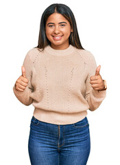 Poster - Young latin girl wearing wool winter sweater success sign doing positive gesture with hand, thumbs up smiling and happy. cheerful expression and winner gesture.