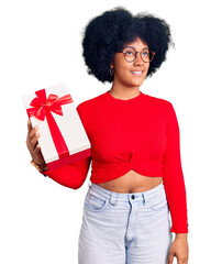 Wall Mural - Young african american girl holding gift smiling looking to the side and staring away thinking.