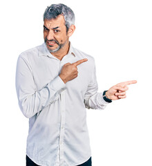 Canvas Print - Middle age hispanic with grey hair wearing casual white shirt pointing aside worried and nervous with both hands, concerned and surprised expression