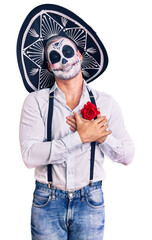 Poster - Man wearing day of the dead costume over background smiling with hands on chest with closed eyes and grateful gesture on face. health concept.