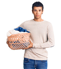 Poster - Young african amercian man holding laundry basket thinking attitude and sober expression looking self confident