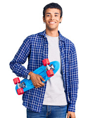 Poster - Young african amercian man holding skate looking positive and happy standing and smiling with a confident smile showing teeth