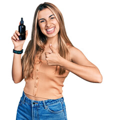 Canvas Print - Hispanic young woman using night serum smiling happy and positive, thumb up doing excellent and approval sign