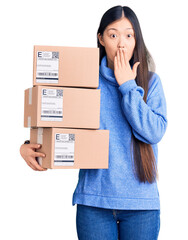 Sticker - Young beautiful chinese woman holding delivery cardboard boxes covering mouth with hand, shocked and afraid for mistake. surprised expression