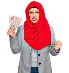 Sticker - Beautiful hispanic woman wearing islamic hijab holding 10 pounds banknotes annoyed and frustrated shouting with anger, yelling crazy with anger and hand raised