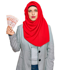 Sticker - Beautiful hispanic woman wearing islamic hijab holding singapore dollars banknotes thinking attitude and sober expression looking self confident