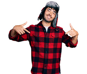 Poster - Hispanic young man with beard wearing fluffy earmuff hat looking confident with smile on face, pointing oneself with fingers proud and happy.