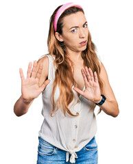 Young caucasian woman wearing casual style with sleeveless shirt moving away hands palms showing refusal and denial with afraid and disgusting expression. stop and forbidden.