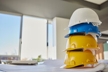 Building, Helmets And Architect Equipment On Table For Construction Safety, Security Or Industrial Work Gear At Office. Stack Of Hard Hats On Desk For Safe Engineering Or Contracting For Architecture