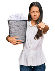 Sticker - Beautiful hispanic woman holding paper bin full of crumpled papers pointing with finger to the camera and to you, confident gesture looking serious