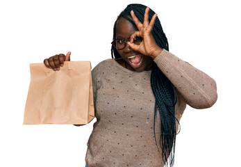 Poster - Young black woman with braids holding take away paper bag smiling happy doing ok sign with hand on eye looking through fingers