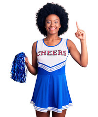 Sticker - Young african american woman wearing cheerleader uniform holding pompom smiling amazed and surprised and pointing up with fingers and raised arms.