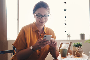 Canvas Print - Welcome to the digital age. Cropped shot of an attractive young businesswoman sitting alone in her home office and texting on her cellphone.