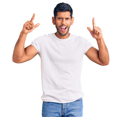 Sticker - Young latin man wearing casual clothes smiling amazed and surprised and pointing up with fingers and raised arms.