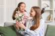 © Pixel-Shot - Cute little girl greeting her mother with flowers at home on holiday
