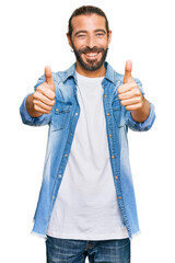 Wall Mural - Attractive man with long hair and beard wearing casual denim jacket success sign doing positive gesture with hand, thumbs up smiling and happy. cheerful expression and winner gesture.