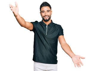 Canvas Print - Young man with beard wearing sportswear looking at the camera smiling with open arms for hug. cheerful expression embracing happiness.