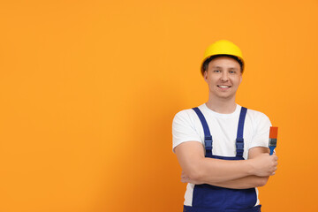 Canvas Print - Happy worker holding paint brush near orange wall. Space for text