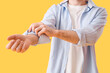© Pixel-Shot - Young man rolling up his sleeve on yellow background, closeup