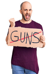 Canvas Print - Young handsome man holding prohibited guns banner screaming proud, celebrating victory and success very excited with raised arms