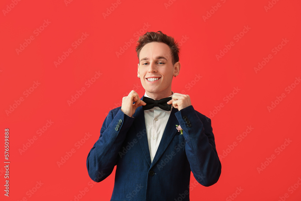 Young man in prom suit adjusting bow on red background