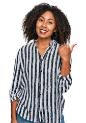 Young african american girl wearing casual clothes smiling with happy face looking and pointing to the side with thumb up.