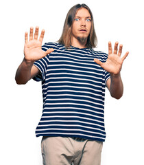 Poster - Handsome caucasian man with long hair wearing casual striped t-shirt afraid and terrified with fear expression stop gesture with hands, shouting in shock. panic concept.